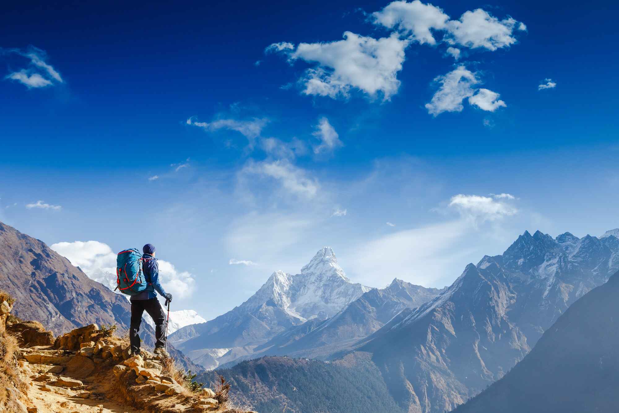 Image of a hiker standing on the side of a mountain looking towards some mountain peaks in the distance