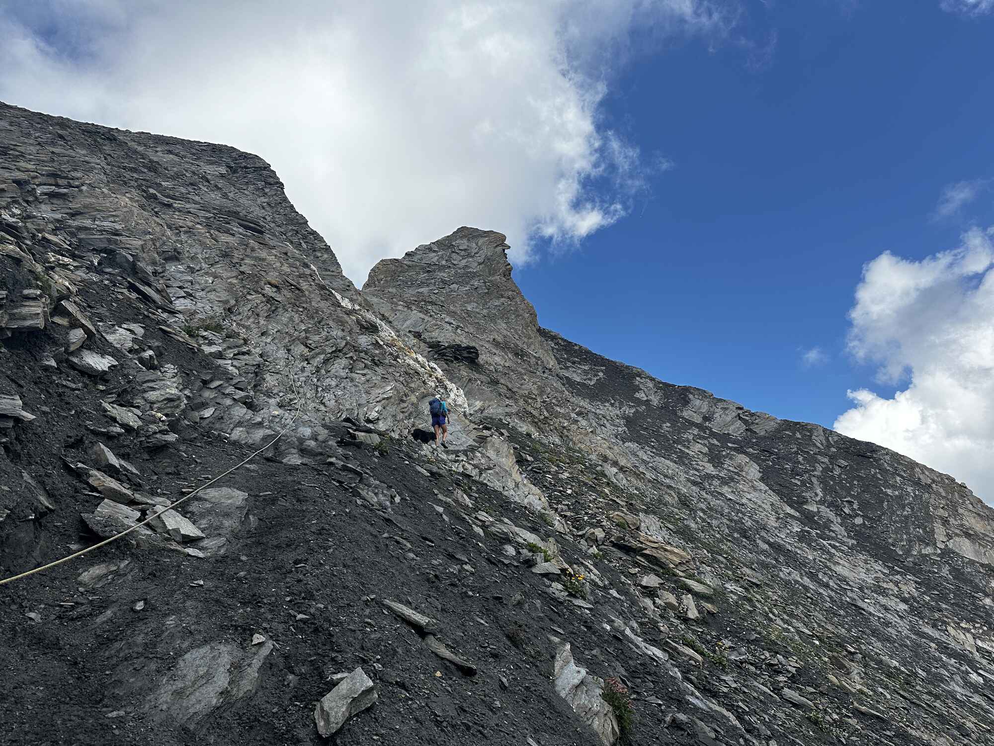 Person with a dog walking along a trail of rouck in the mountains